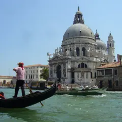 Gondolier wita turystów w Wenecji. W tle Bazylika Santa Maria della Salute i kanał.