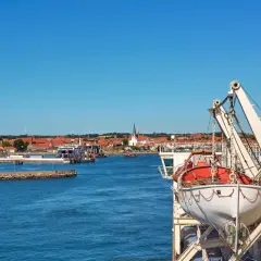 Widok na port z promem, łodzią ratunkową i miastem w tle.