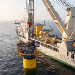 Statek z dźwigiem instaluje żółty fundament morskiej farmy wiatrowej na wodzie.