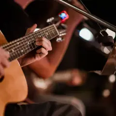 Ręce grające na gitarze akustycznej, w tle migoczą światła, tworząc atmosferę jak na stena line dyskotece.