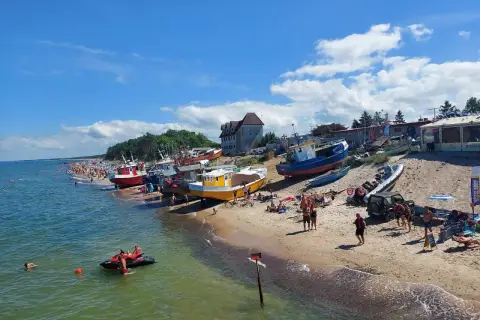 Słoneczne **morze bałtyckie wakacje** z kolorowymi łodziami na plaży i tłumem ludzi cieszących się słońcem.