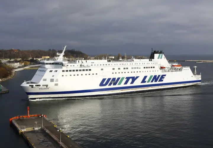 Biały prom Unity Line "Polonia" płynie po wodzie, w tle widać port i zachmurzone niebo.