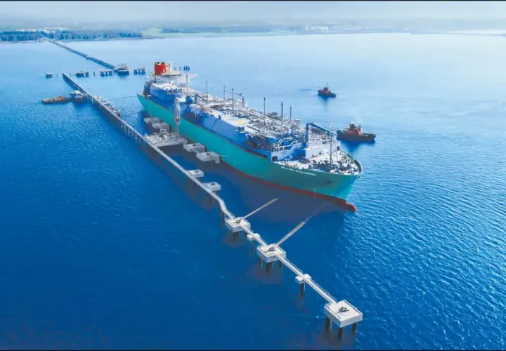 Pływający terminal LNG przycumowany do nabrzeża, z holownikami na wodzie.
