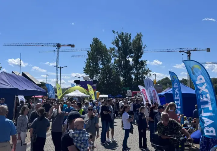 Tłum ludzi na zewnątrz, namioty, flagi i dźwigi w tle.